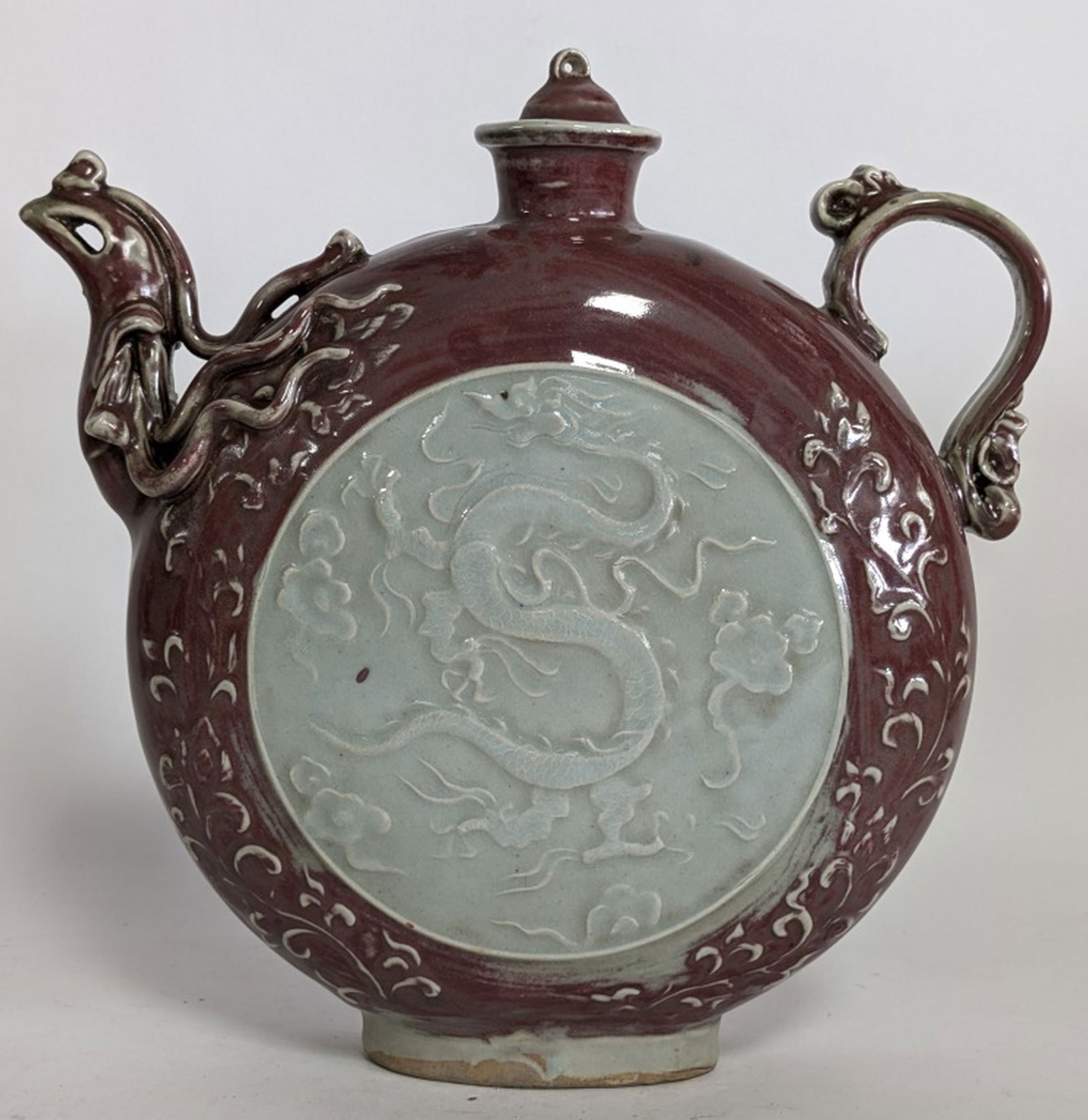 Antique Chinese Celadon Dragon Moon Flask 10.75"H: Chinese celadon moon flask or pilgrim's flask with a carved dragon motif. 10.75"H x 11W x 3D". The flattened, circular form is characteristic of a moon flask, a shape derived from ancient metal and le