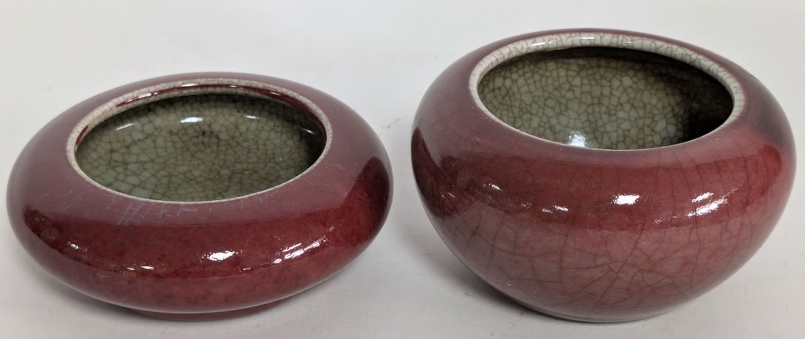 Antique Chinese Oxblood Brush Washer Water Pots: Chinese red-glazed porcelain water pots, often referred to as oxblood or sang de boeuf. Large pot: 2.5H x 4.5W in. Small pot: 1.75H x 4.5W in. The vibrant red color is achieved using a complex copper-