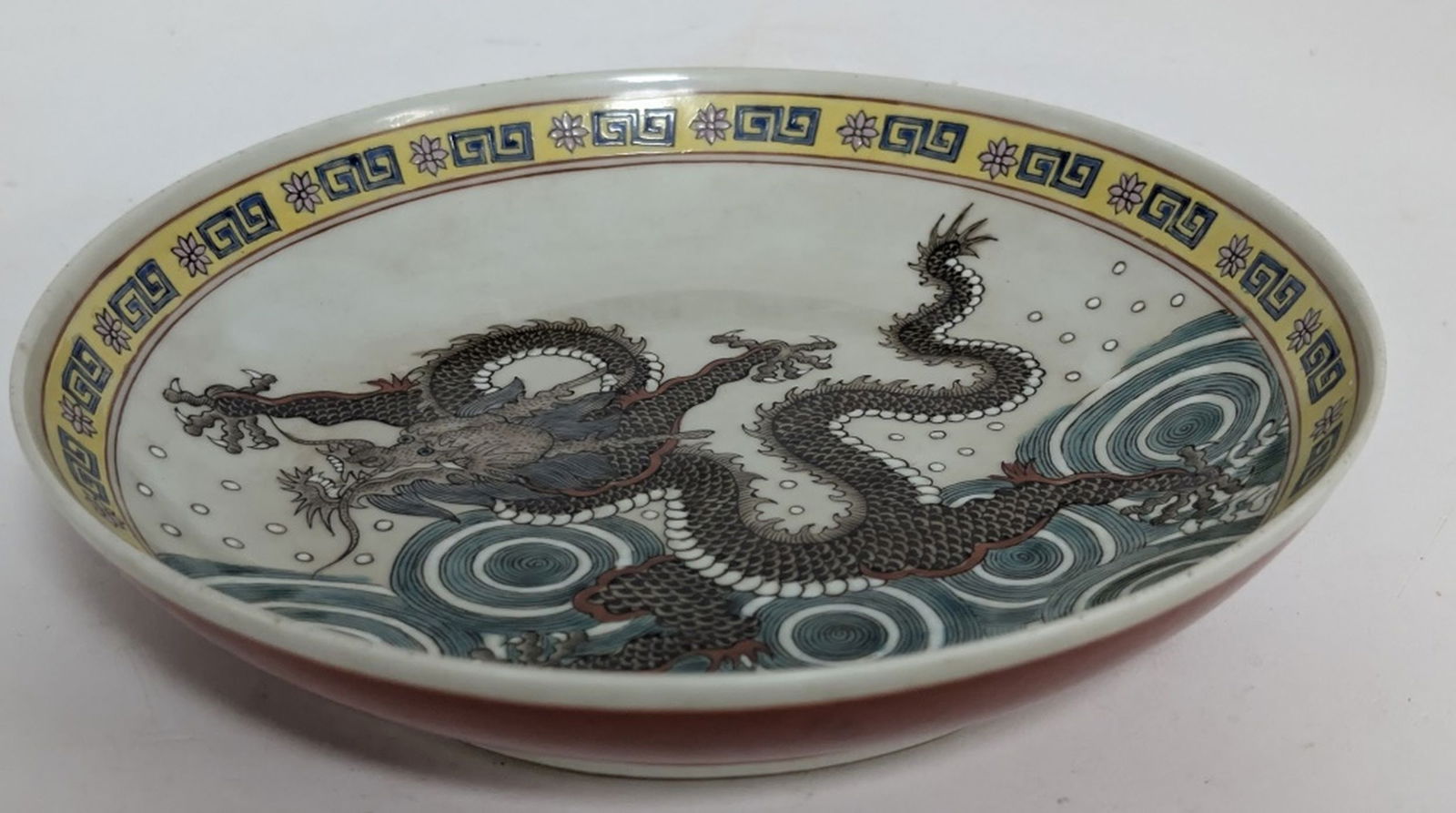 Jingdezhen Qinghua Handpainted Dragon Dish 8.75W": Excellent Jingdezhen Qinghua Handpainted Dragon Dish. 8.75W x 1.75H in. It features a hand-painted black and grey dragon motif over a background of swirling waves. The rim has a yellow border with a r