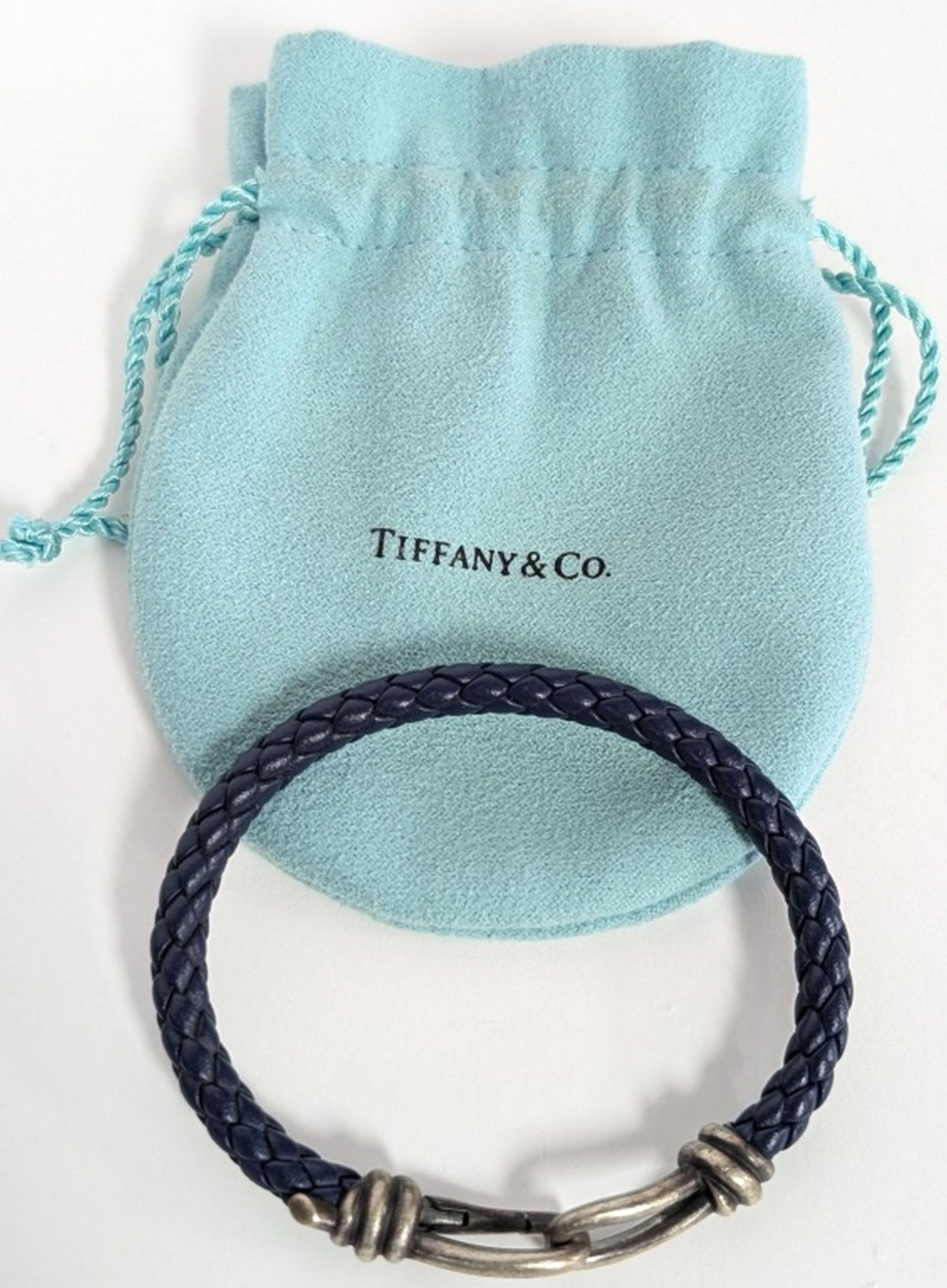 Tiffany & Company Silver & Leather Hook Bracelet: Tiffany & Co. Sterling Silver and Blue Braided Leather Hook Bracelet. A stylish and recognizable Tiffany & Co. bracelet featuring a richly colored blue braided leather band terminating in Tiffany's si