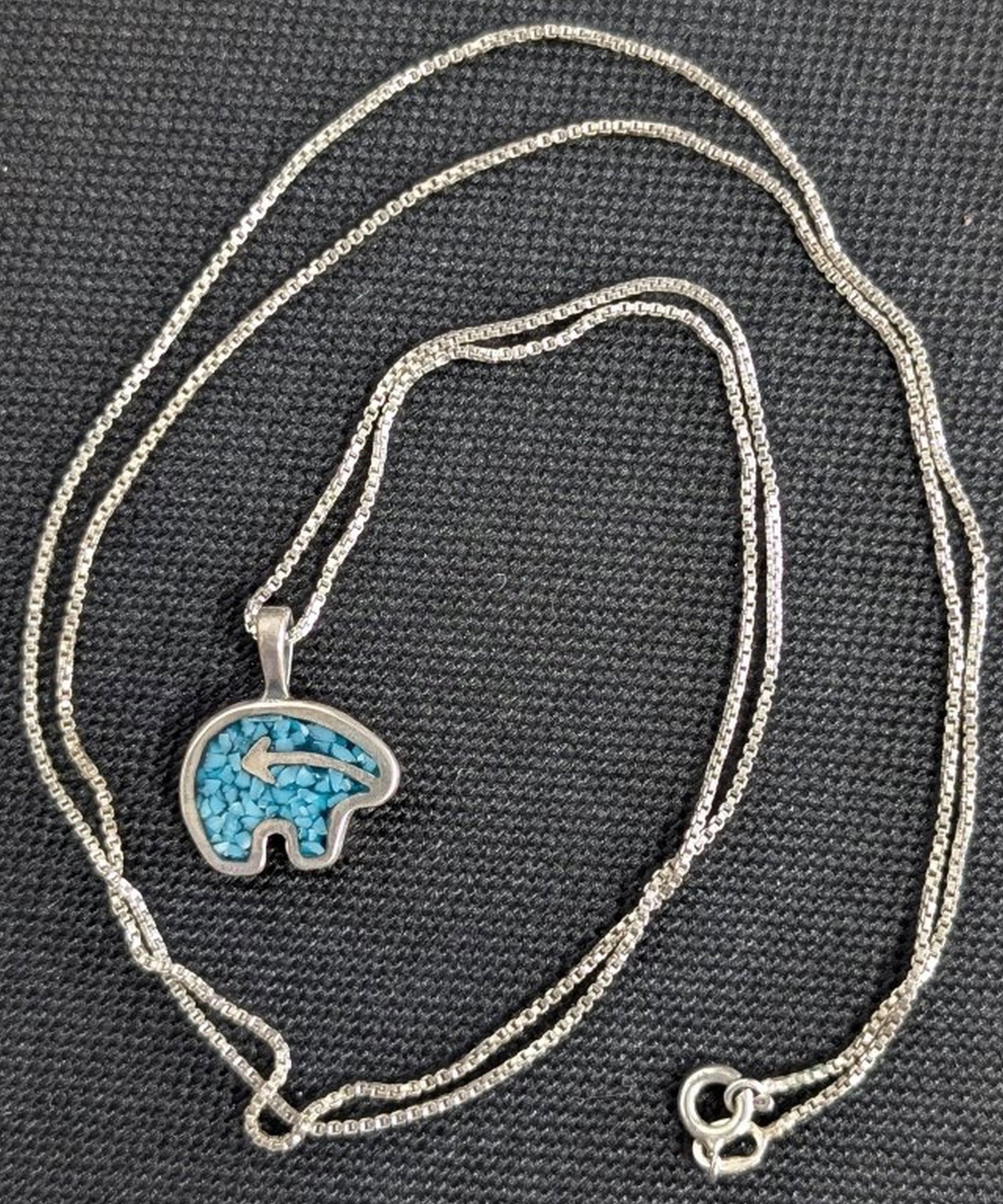 Sterling Silver Turquoise Bear Pendant Necklace: Delightful sterling silver necklace featuring a stylized bear-form pendant with vibrant turquoise chip inlay and an applied arrow motif. The pendant is stamped .925 to the reverse and is suspended fro