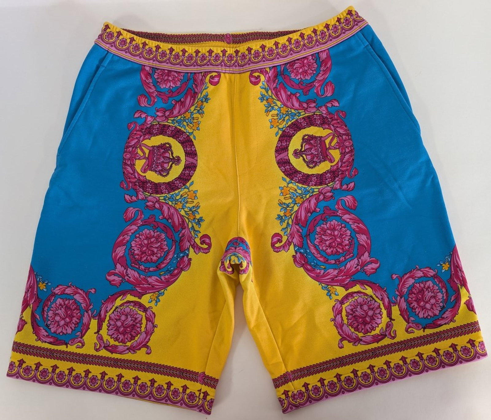 Versace Baroque Print Knit Shorts: Boldly patterned Versace shorts featuring a vibrant Baroque-inspired print in turquoise blue, yellow, and pink with Medusa and scrollwork motifs. Constructed with an elastic waistband and side-seam po