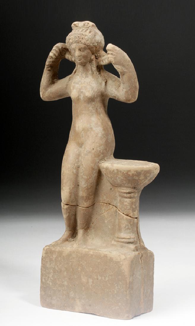 Greek Terracotta Statue of Aphrodite: Greece, Hellenistic period, ca. 4th to 3rd centuries BCE. An earthenware votive figure of the goddess Aphrodite, mold-made and hollow. She stands on a cube pedestal, nude, with her arms raised, holdin