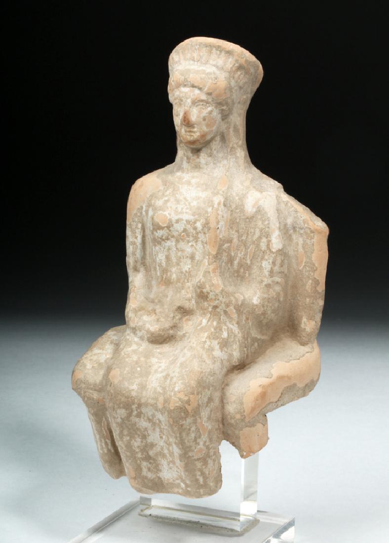 Western Greek Earthenware Seated Woman: Western Greece, Archaic period, ca. 7th century BCE. A mold made, hollow votive figure depicting a woman seated on a wide throne. The woman wears a wide, crown-like headdress and her clothing is drape
