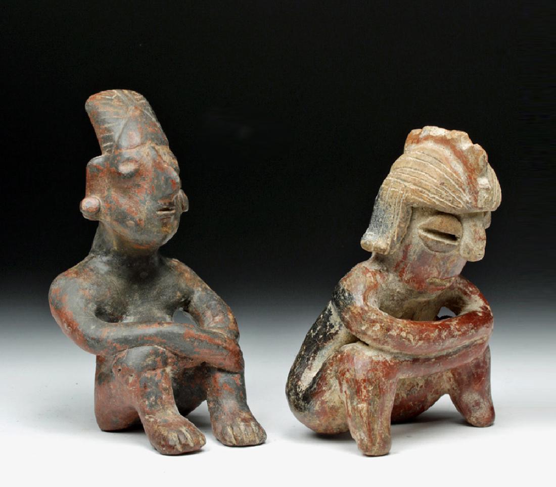 Pair of Jalisco Ceramic Seated Figures: Pre-Columbian, West Mexico, Jalisco, ca. 300 BCE to 300 CE. A pair of earthenware seated figures, both leaning forward, elbows on their knees. One has a dramatic, crested coiffure and coffee-bean styl