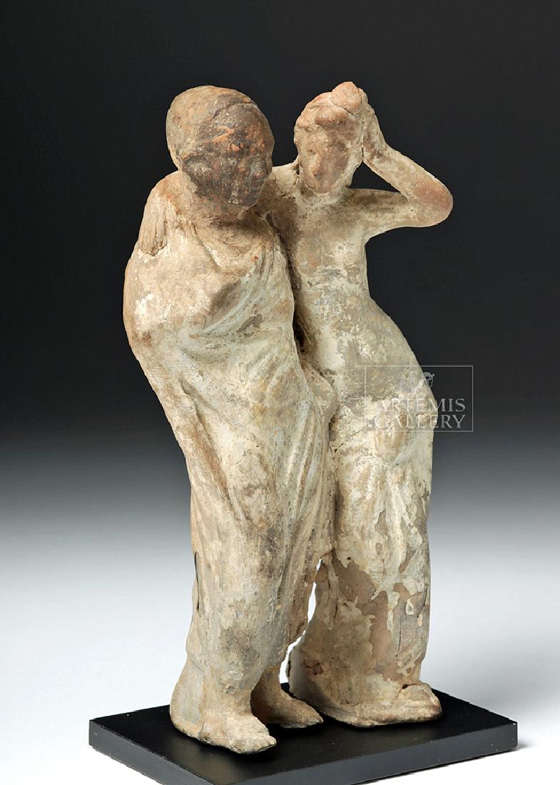 Greek Tanagra Pottery Standing Couple: Greece, Hellenistic period, ca. 3rd century BCE. A mold-made ceramic standing figure depicting an older man, wrapped tightly in his clothing so that only his face and feet are exposed, and a woman, nu
