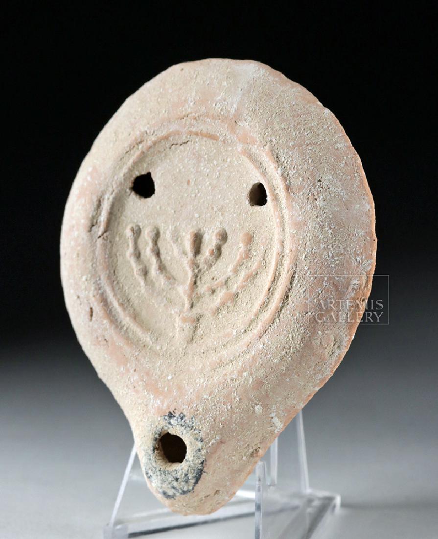 Roman Terracotta Oil Lamp w/ Jewish Menorah: Roman, Imperial Period, ca. 1st to 3rd century CE. A mold-made terracotta oil lamp of a petite composition with a concentric ring base, gently-sloping walls, rounded shoulders, twin fill holes, and a 