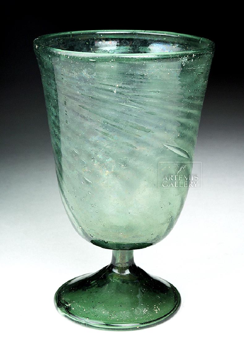 Roman / Byzantine Glass Goblet, ex-Charles Ede: Roman, late Imperial / early Byzantine periods, ca. 5th to 8th century CE. A beautiful free-blown green glass goblet with a wide foot and short leg, a gently flaring body, a deep cavity, and a rolled 