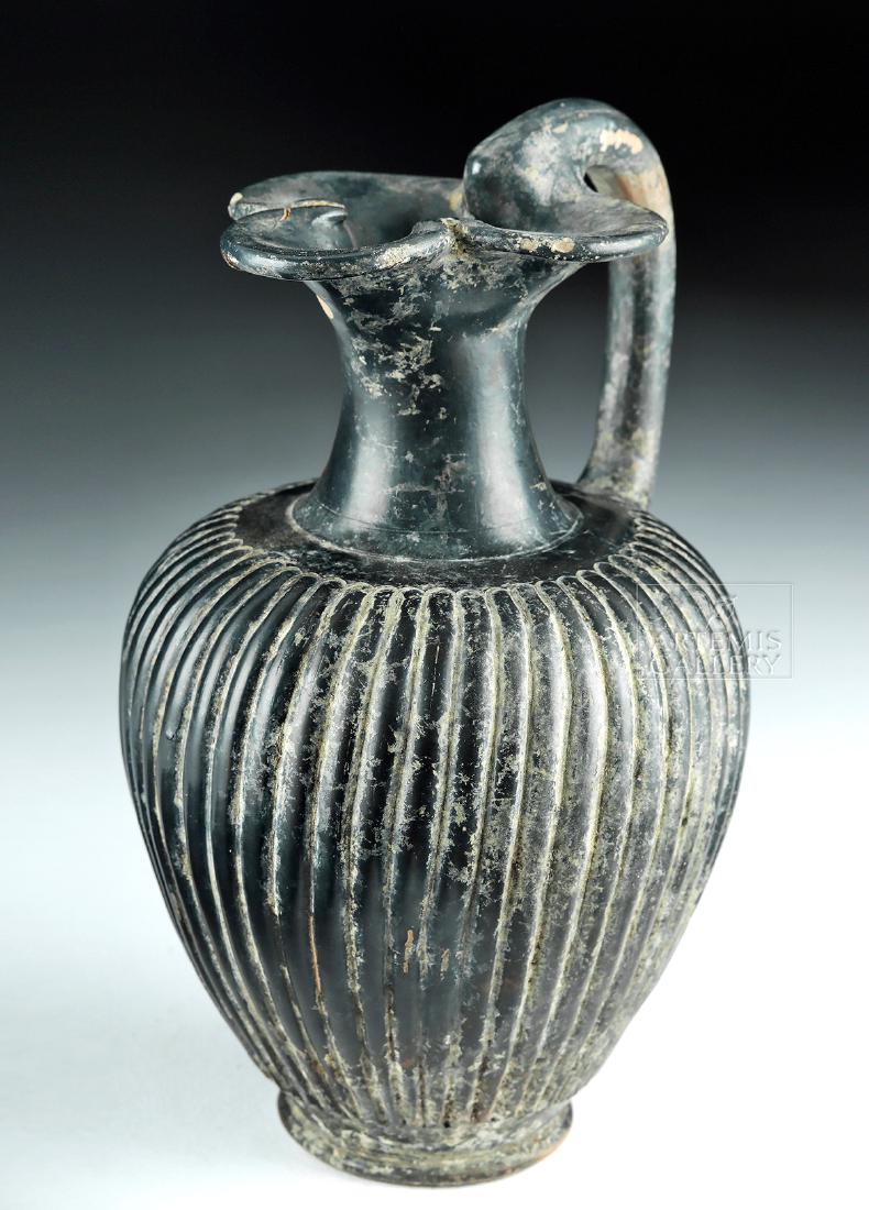 Greek Apulian Black Glazed Oinochoe w/ Trefoil Lip: Magna Graecia, Southern Italy, Apulia, ca. early 4th century BCE. A pretty oinochoe (pouring vessel) with a trefoil lip and a delicate arched handle bridging rim to shoulder. Its piriform body stands 