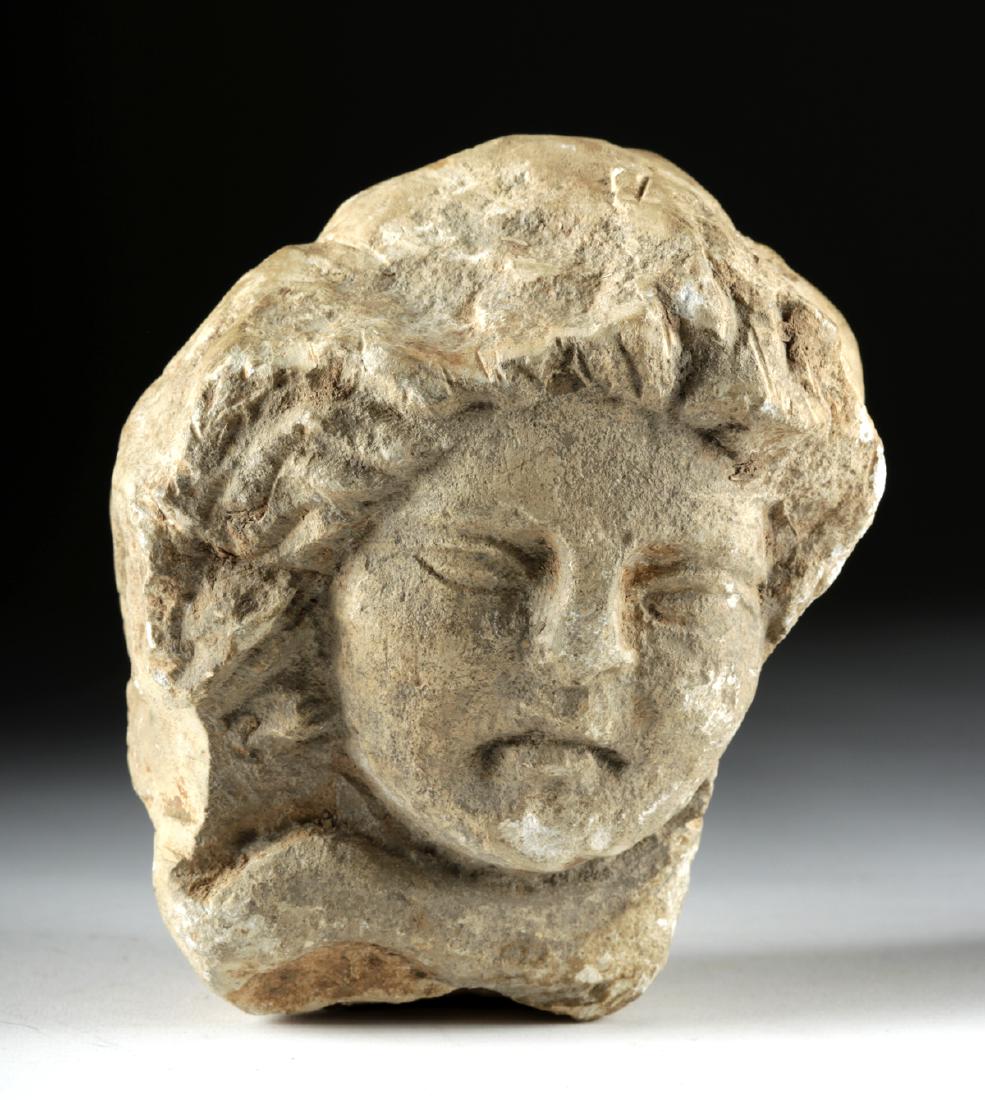 Provincial Roman Carved Marble Head: Roman provinces, Imperial Period, ca. 3rd to 5th century CE. A haunting carved marble head, likely from a memorial. The head is surrounded by flowing hair and has beautifully symmetrical features with