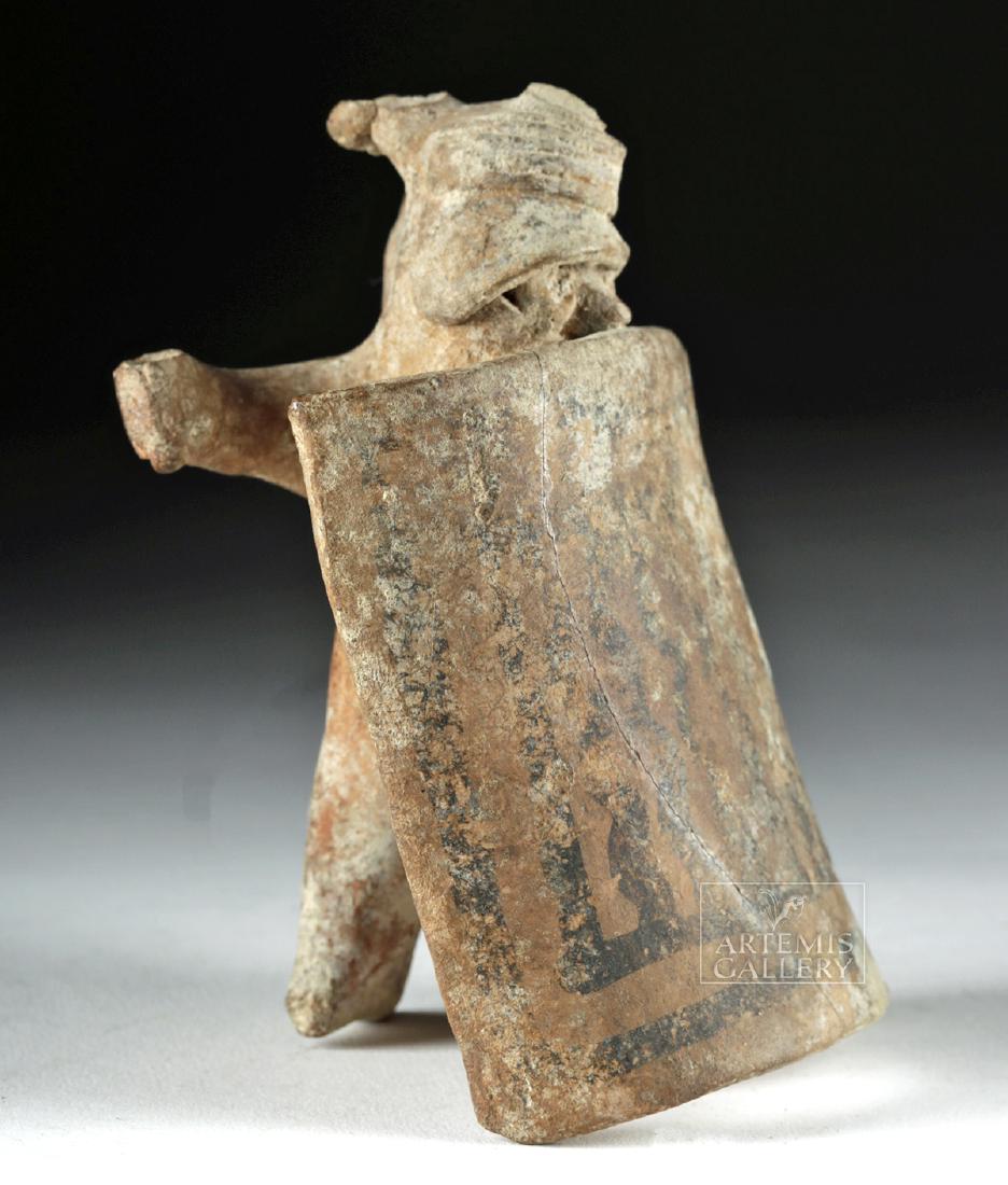 Colima Pottery Standing Warrior w/ Shield: Pre-Columbian, West Mexico, Colima, ca. 300 BCE to 300 CE. A charming, hand-built pottery warrior figure standing behind a massive convex shield decorated with faded black-painted linear motifs. The f