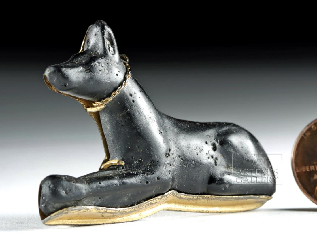 Egyptian Black Glass Anubis w/ Gold Tone Setting: Egypt, Late Dynastic Period, 26th to 30th Dynasties, ca 672 to 343 BCE. A large ancient black glass amulet in the form of a reclining Anubis depicted in his natural jackal form and mounted on a 20th c