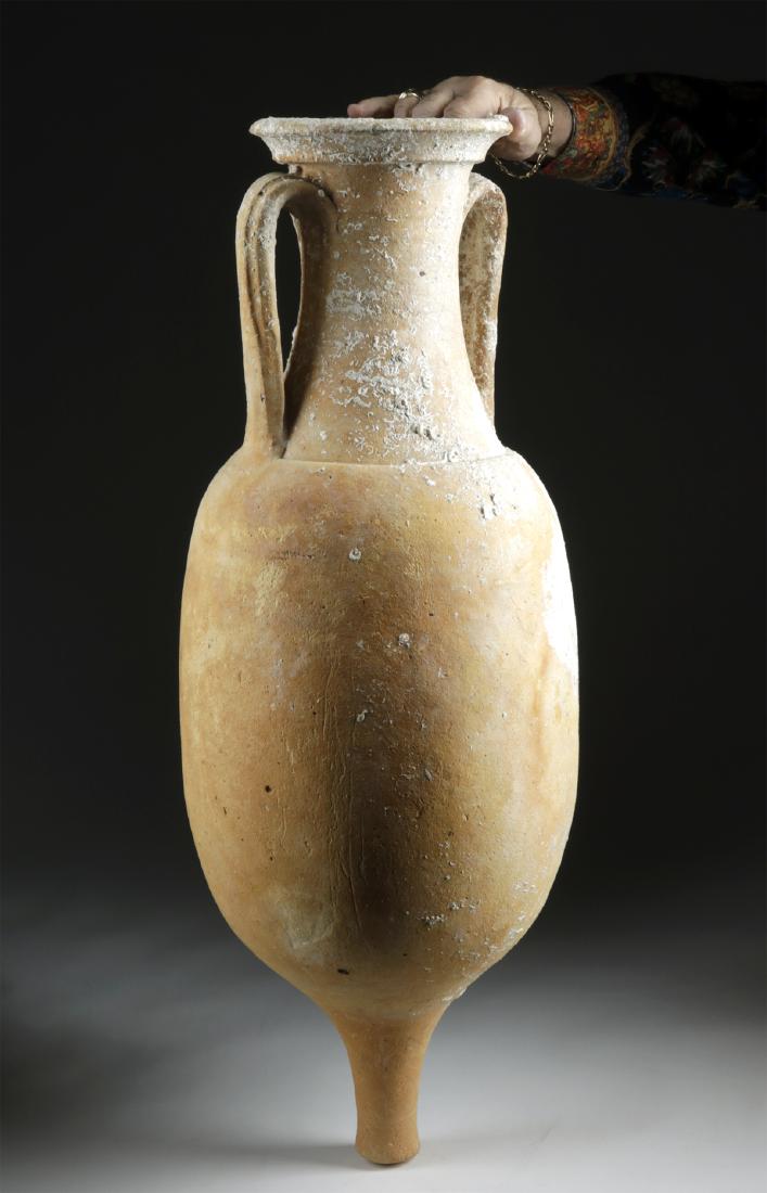 Large Roman Pottery Transport Amphora: Roman, Imperial Period, ca. 2nd to 4th century CE. A fine pottery transport amphora with a narrow conical base, a smooth globular body, rounded shoulders with a slightly corseted neck base, a thick cy