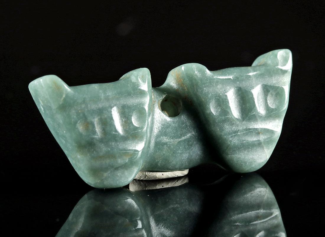 Costa Rican Jade Amulet w/ Double Jaguar Faces: Pre-Columbian, Costa Rica, ca. 500 to 1200 CE. A skillfully carved and string cut jadeite amulet depicting twin jaguar warrior visages with stylized facial features and feline ears - perforated throug