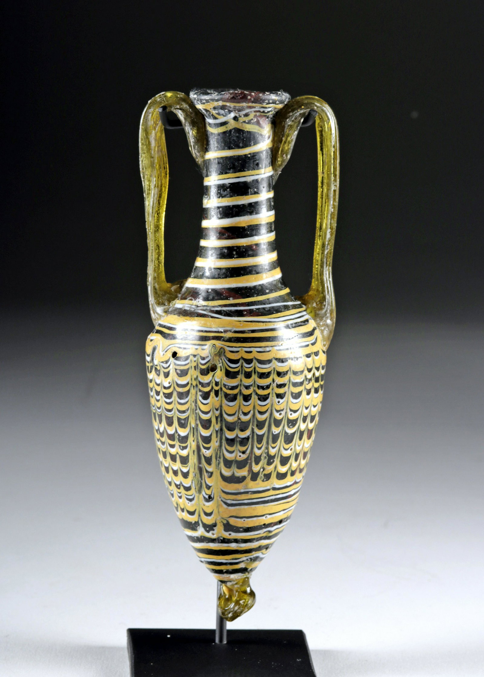 Large Greek Core Formed Amphora: Ancient Greece, Classical Period, ca. 2nd to 1st century BCE. Comprised of a deep forest green glass body with opaque yellow and white trailing wrapped around the neck and shoulder, a feathered patter