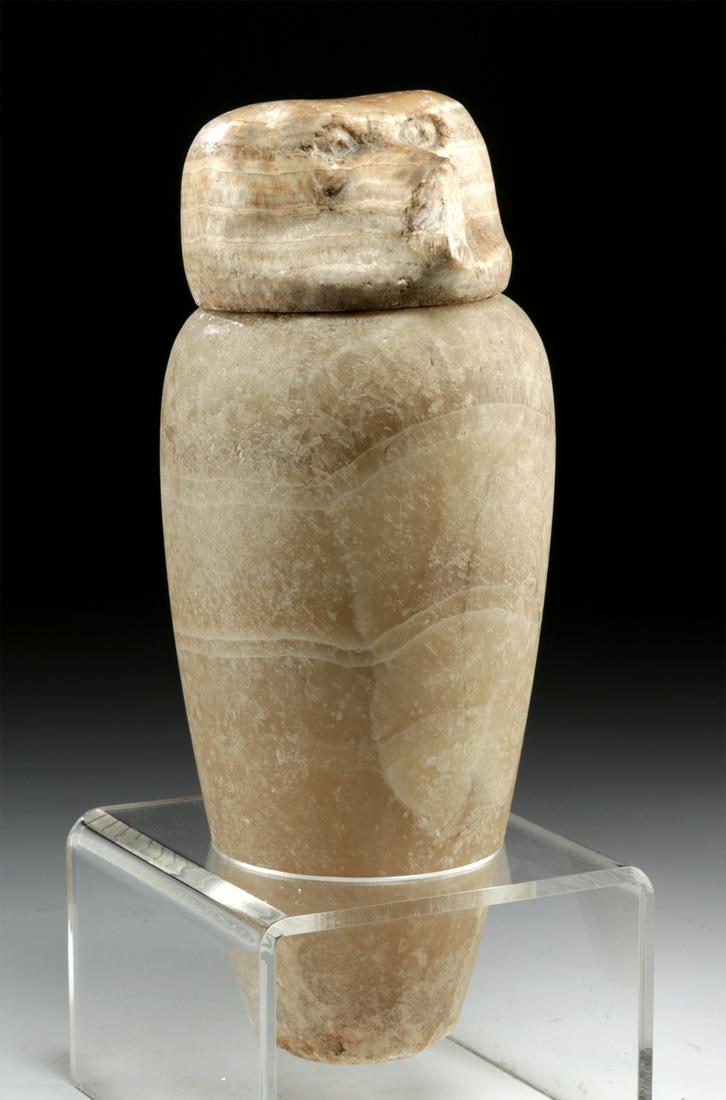Egyptian Calcite Alabaster Canopic Jar w/ Baboon Lid: Egypt, Late Dynastic Period, 26th to 31st Dynasty, ca. 664 to 332 BCE. A handsome canopic jar, hand-carved from honey-yellow calcite alabaster with natural veins that illuminate when held next to a br