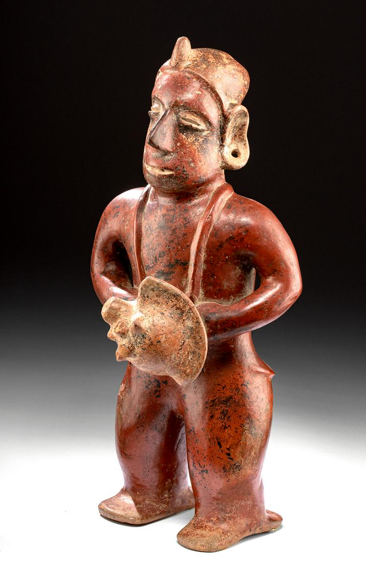 Colima Pottery Standing Warrior with Conch Shell: Pre-Columbian, West Mexico, Colima, ca. 300 BCE to 300 CE. An impressive hand-modeled redware standing musician, holding a large conch shell instrument that is suspended around his neck in both hands.