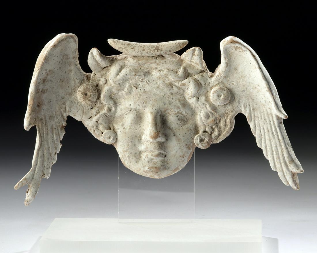 Greek Canosan Pottery Winged Head Applique: Magna Graecia, Apulia, Canosan Hellenistic Period, ca. 4th to 3rd century BCE. A fascinating ceramic applique of a winged head, made to adorn a large vessel like an amphora. The head is that of either