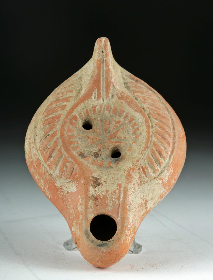 Byzantine Pottery Oil Lamp with Christogram: **First Time At Auction** Near East/Holy Land, Byzantine Empire, ca. 4th to 5th century CE. An iron-rich ceramic lamp with a round, disc-like body, two filler holes, a pointed handle, and an elongated