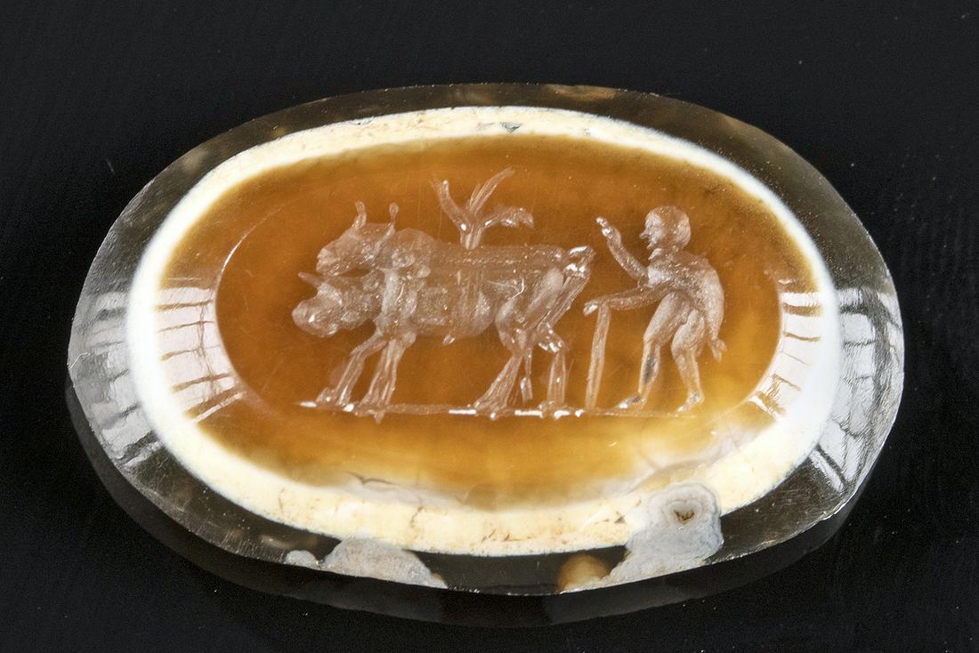 Roman Banded Agate Intaglio - Man with Oxen: Roman, Imperial Period, ca. 2nd to 3rd century CE. A gorgeous ovoid intaglio carved from agate with dark-brown, white, and caramel-hued bands that create a naturally layered presentation. The top is i