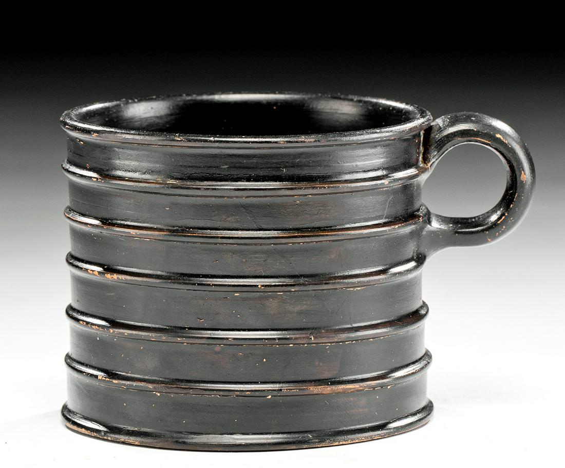 Greek Campanian Glazed Pottery Mug w/ Ribs: Magna Graecia, South Italic Colonies, Campania, ca. 360 to 320 BCE. A fine wheel-thrown pottery mug with a broad base, gently tapered walls ringed with five horizontal ribs, a rounded rim surrounding 