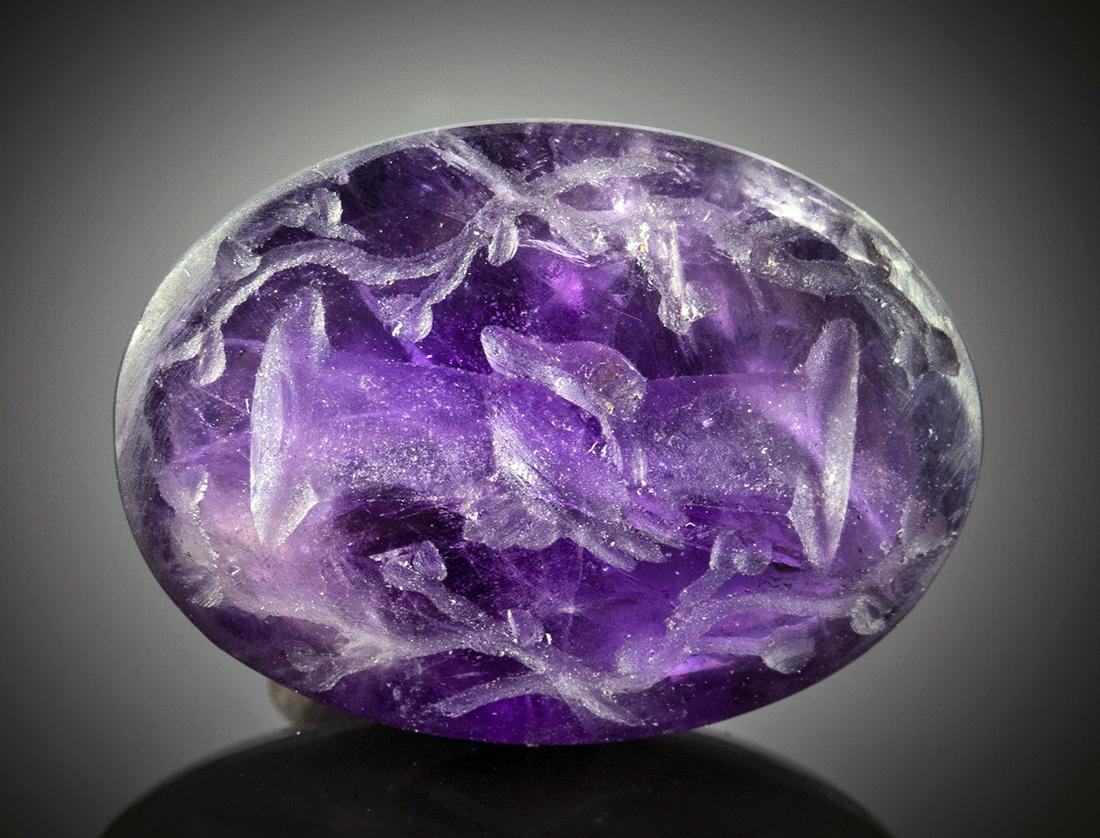 Roman Amethyst Intaglio with Hands Clasped: Roman, Imperial Period, ca. 1st to 4th century CE. A lovely deep purple ovoid amethyst intaglio incised with a scene of two hands grasping each other, surrounded by a border of vines on its flat face.