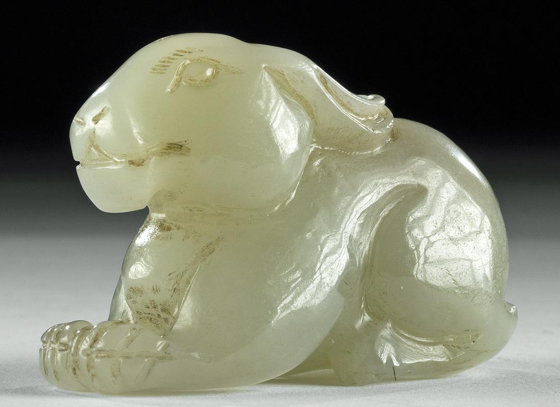 19th C. Chinese Jade Figural of a Prone Bunny: East Asia, China, Qing Dynasty, ca. 19th century CE. A charming three-dimensional jade carving of a seated bunny, its long ears flat along its back and its surface lightly scored to emphasize its fur.