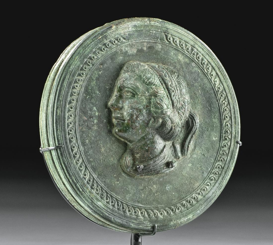 Roman Bronze Mirror w/ Woman's Portrait: Roman, Imperial Period, ca. 1st to 3rd century CE. A striking cast bronze mirror with a decorative verso featuring a lovely high relief portrait of a young woman. Its back has a series of incised conc