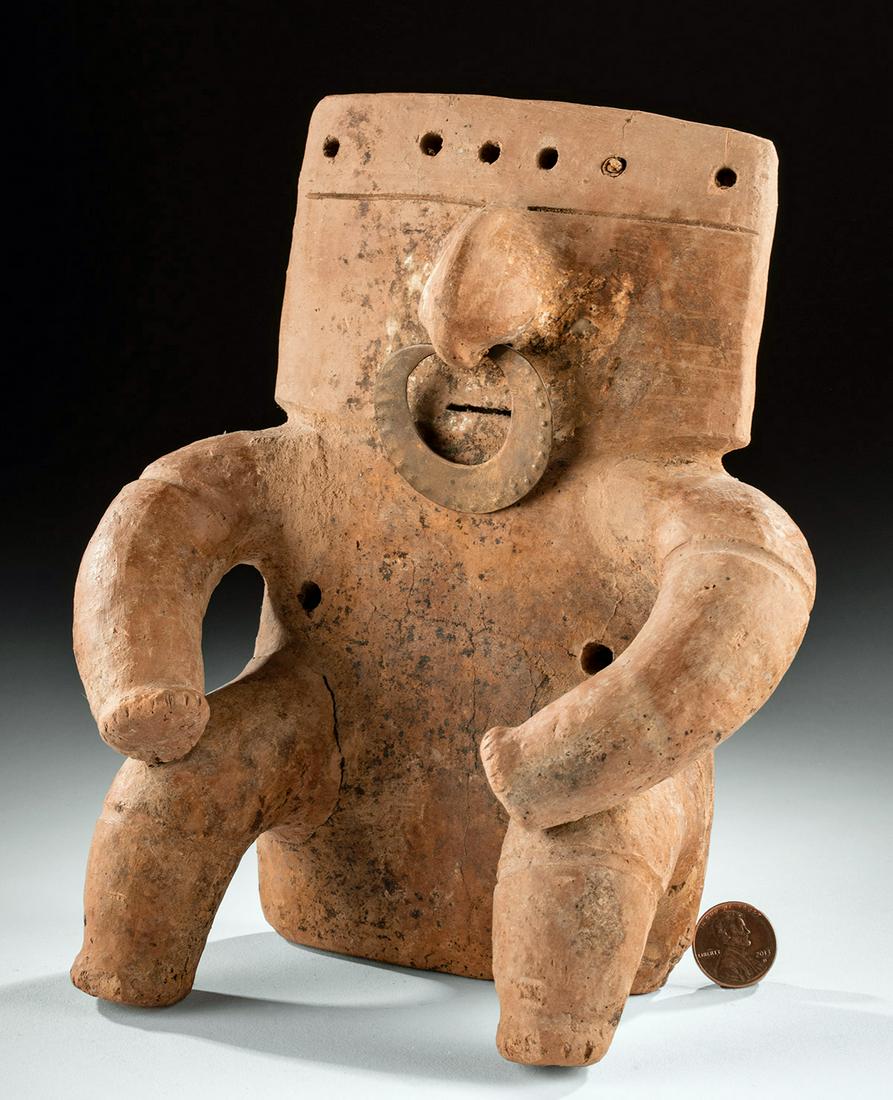Middle Cauca Quimbaya Pottery Figure, Copper Nose Ring: Pre-Columbian, Colombia, Middle Cauca Complex, Quimbaya culture, ca. 800 to 1300 CE. A hollow-built pottery figure of a flat, highly-abstract form seated with bent legs atop a wide base. The curved ar