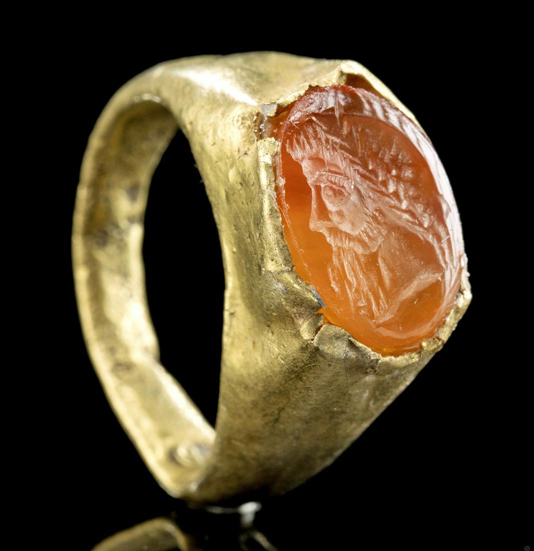 Roman 18K Gold Ring w/ Carnelian Intaglio Jupiter: Roman, Imperial Period, ca. 1st to 3rd century CE. An ancient Roman 75% gold (equivalent to 18K) ring housing a striking carnelian intaglio that is finely carved with the profile visage of a bearded g