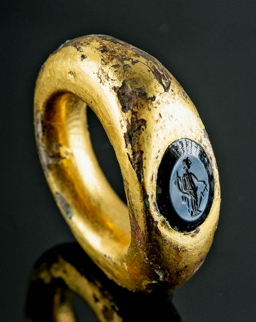 Roman 22K+ Gold, Bronze, & Onyx Intaglio Ring, Fortuna: Roman, Imperial Period, ca. 1st to 2nd century CE. A bronze ring wrapped in 22K gold sheet with an ovoid bezel containing an onyx intaglio depicting Fortuna. The dark stone contrasts beautifully with 