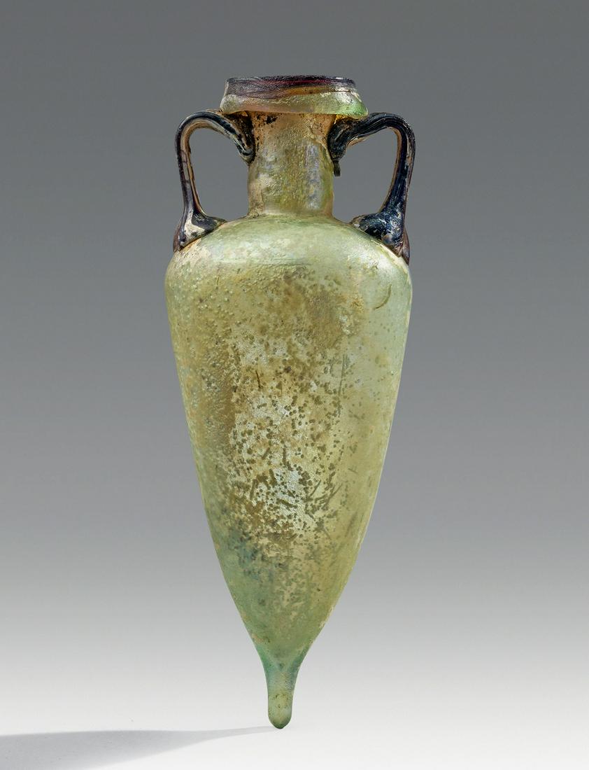 Beautiful Roman Glass Two-Handled Amphoriskos: Roman empire, ca. 1st century CE. The classic amphora-shaped (hence the name amphoriskos or little amphora). Blown using natural, pale greenish glass, this bottle has the shape of an amphora, with the