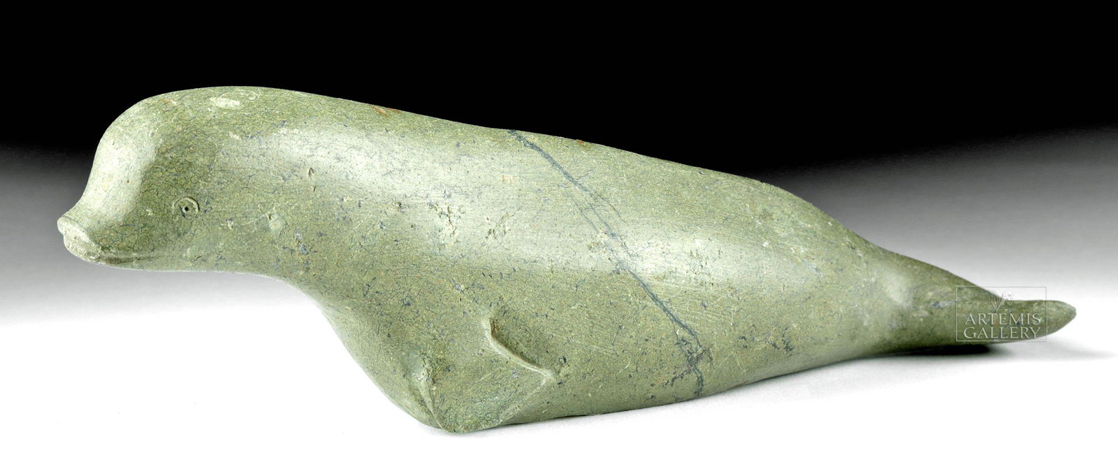 20th C. First Nations Inuit Greenstone Beluga Whale: Native American / First Nations, northern Canada, Inuit, ca. 1950s CE. A delightful deep grey and grey-green stone carving of a beluga whale, its body elongated as if it is in the act of swimming thro