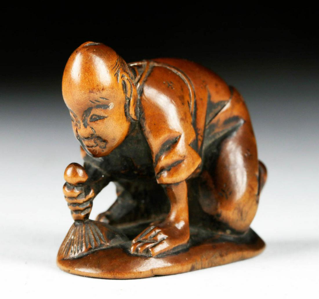 Japanese Boxwood Netsuke - Sweeping Man: East Asia, Japan, Meiji Period, ca. 1868 to 1912 CE. A charming boxwood netsuke in the form of a kneeling man in the act of sweeping, a three-dimensional carving that offers a glimpse into the world o
