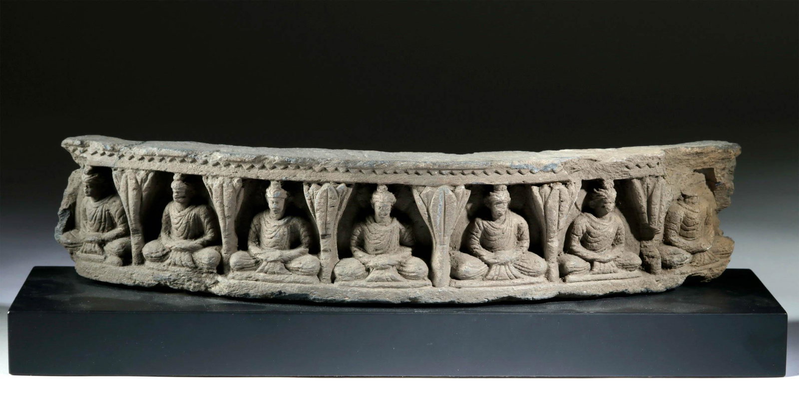 1st C. Gandharan Schist Curved Relief - Seated Buddhas: Central Asia, Pakistan, India, and Afghanistan, Gandharan Empire, ca. 1st century CE. A long, gently curved panel section, perhaps from the base of a stupa or column. It is carved with a series of hig