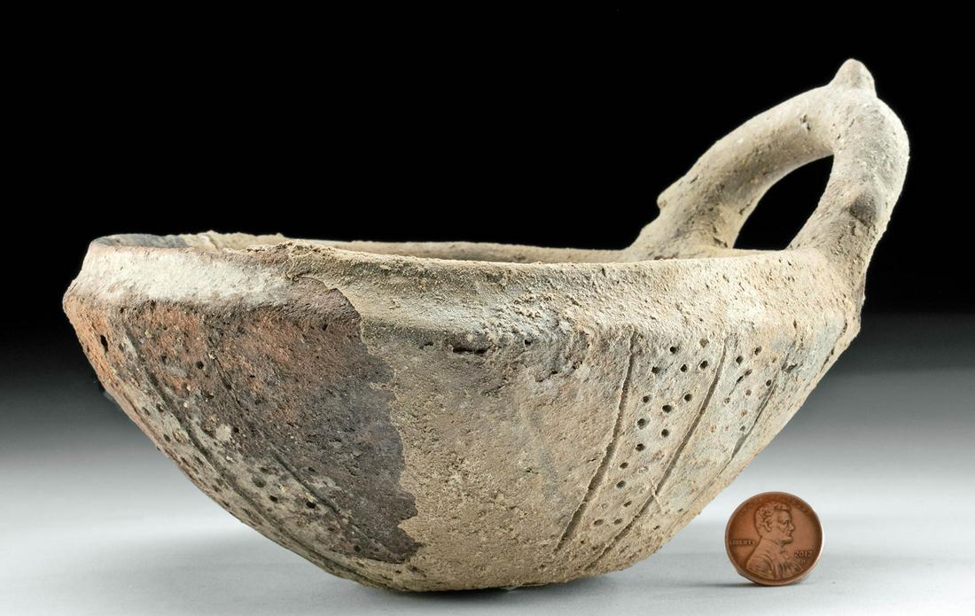 Cypriot Pottery Bowl with Handle and Incised Design: Greece, Cyprus, Middle to Early Late Bronze Age, ca. 1750 to 1550 BCE. A thin, light, and petite pottery handled vessel with a rounded base, thin walls and rim, and a parabolic handle. The body featur