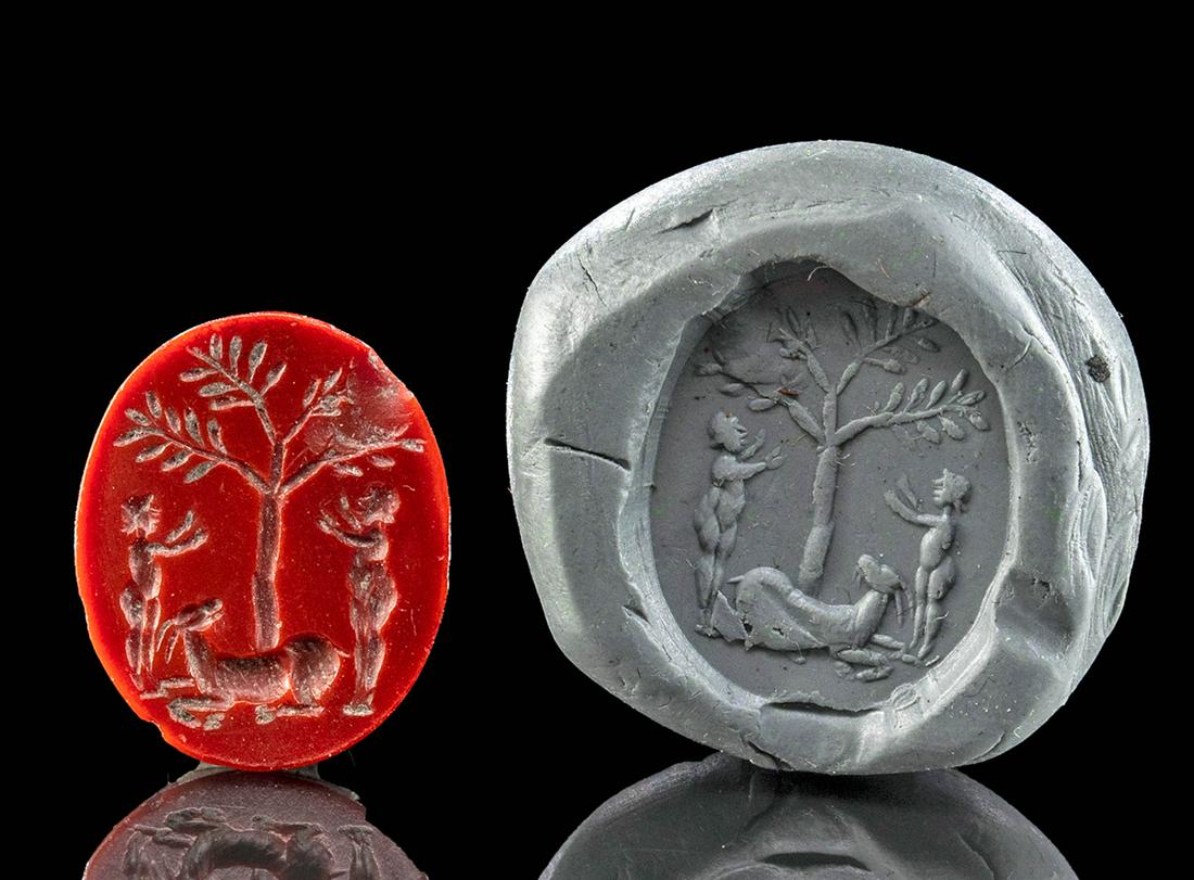 Roman Red Jasper Intaglio of Figures Under a Tree: Roman, Imperial Period, ca. 1st to 3rd century CE. A beautiful deep, wine red jasper intaglio depicting a Bacchanalian scene of two nude figures, each wearing a laurel wreath, standing and facing a ta