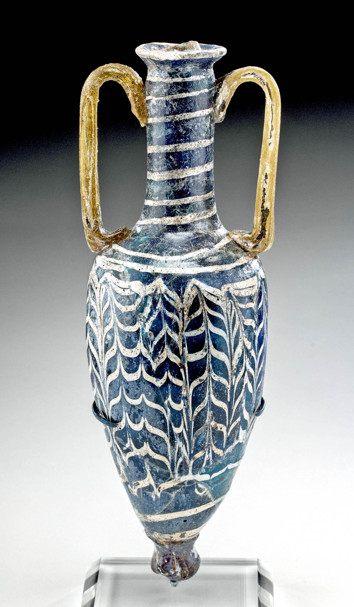 Greek Hellenistic Coreform Glass Amphoriskos: Ancient Greece, Hellenistic, ca. 3rd to 1st century BCE. A beautiful example of a core-formed glass amphoriskos (miniature amphora) once used to hold perfumed oil. This vase boasts an exceptionally el