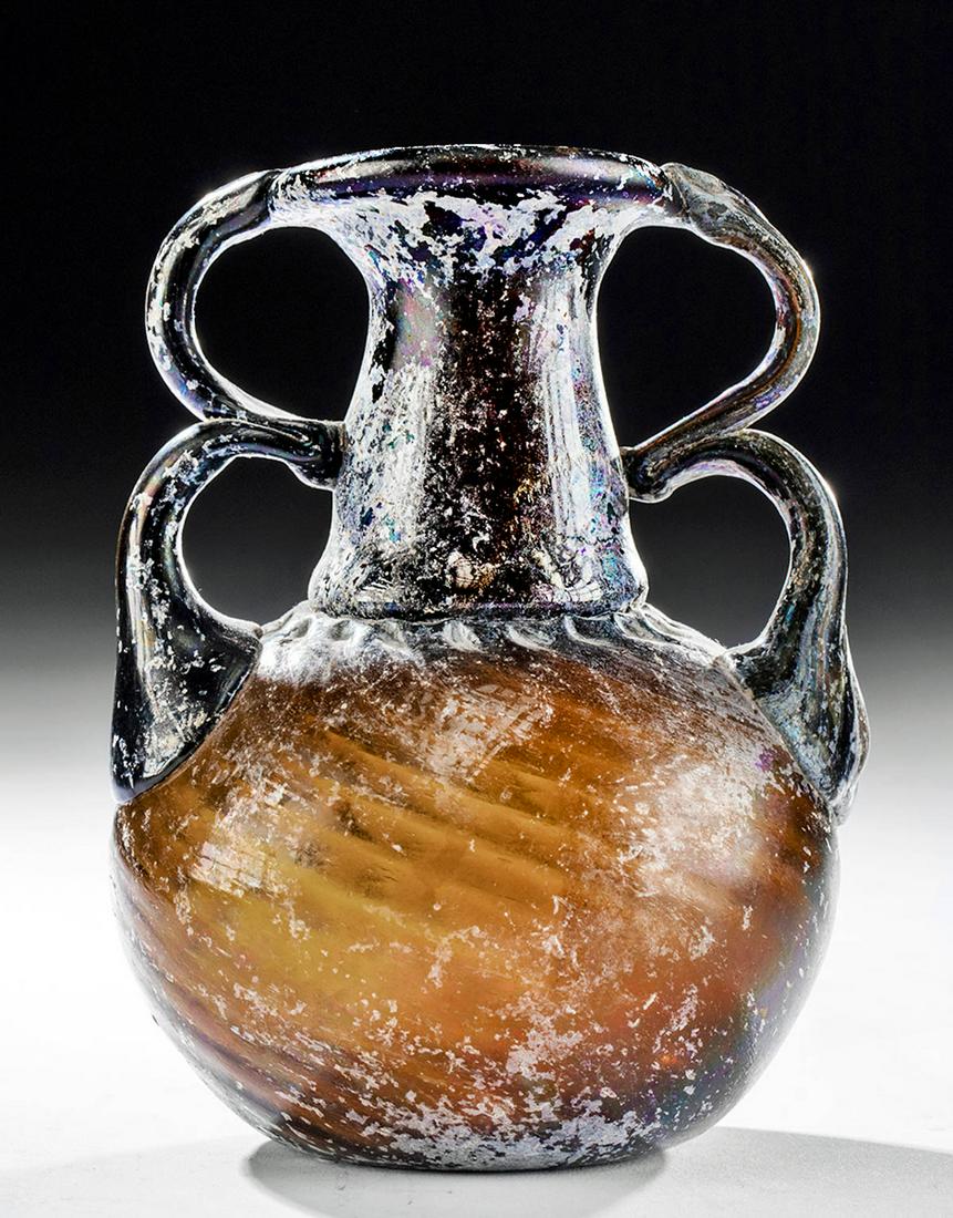 Fine Roman Glass Sprinkler Flask w/ Twin Handles: Roman, Imperial Period, ca. late 1st to 2nd century CE. A gorgeous sprinkler flask of a delicate form, mold-blown from semi-translucent glass of a sumptuous amber hue. The vessel is defined by a conca