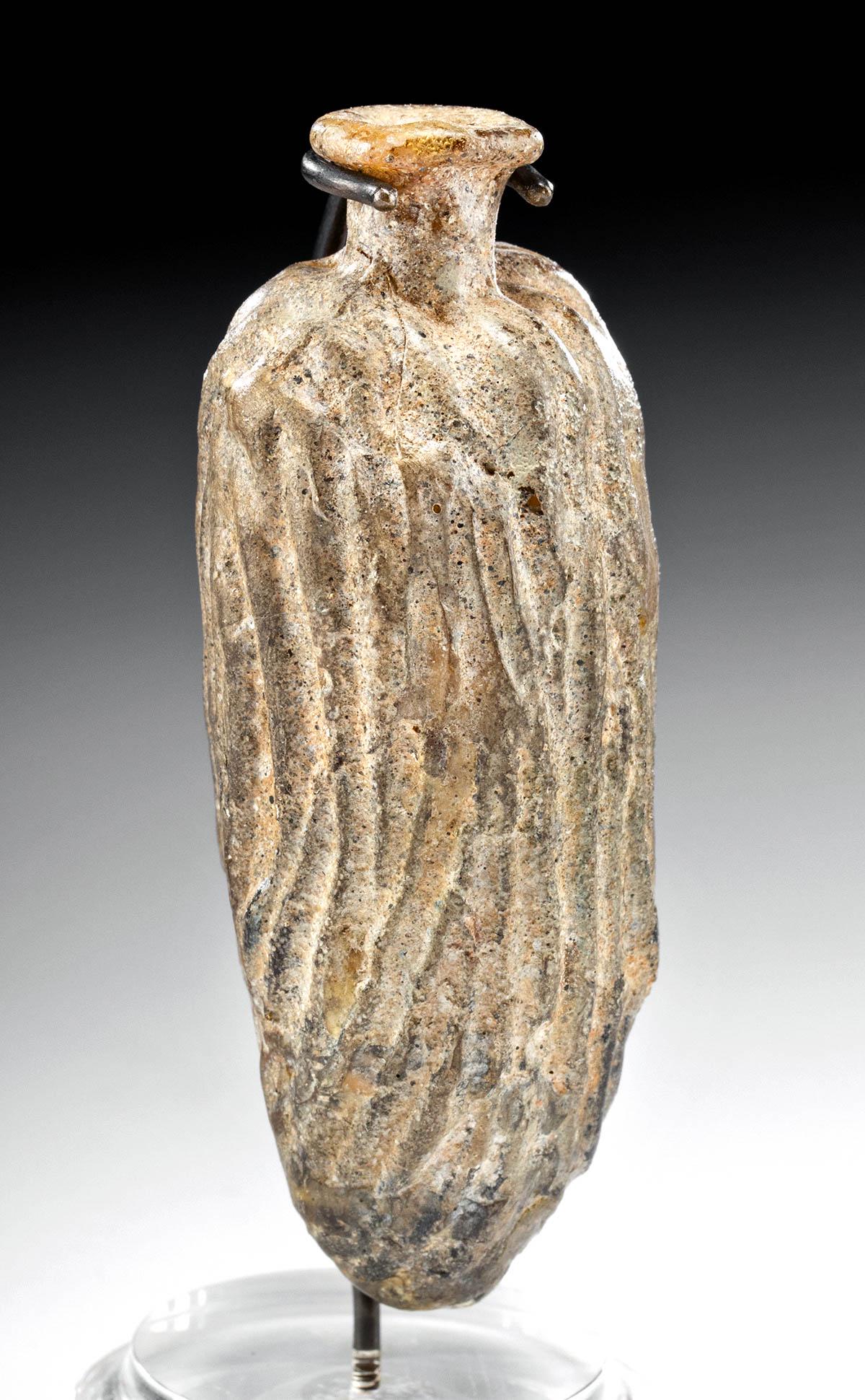 1st C. Sidonian Molded Glass Date Flask: Roman Empire, Lebanon, Sidonian, ca. 1st century CE. A fine mold blown flask resembling a date fruit in amber glass with hints of aubergine - its generally oblong form with a short neck and a flaring