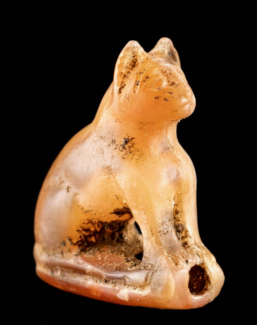 Egyptian Carnelian Bead - Cat / Bastet Amulet: Ancient Egypt, Late Dynastic period, ca. 712 to 332 BCE. This dainty hand-carved and hand-drilled carnelian bead is a beautiful vermillion hue with swirls of white inclusions. Seated on its haunches, 
