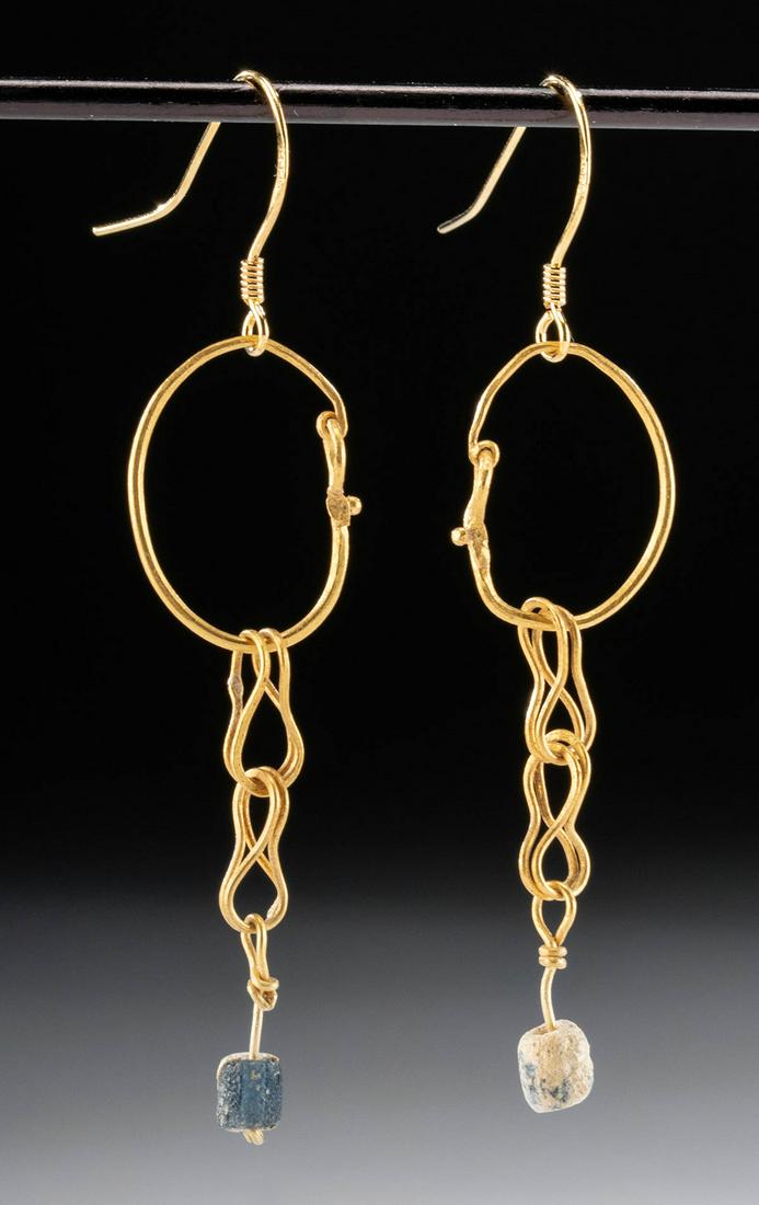 Roman 23K+ Gold Earrings w/ Glass Beads (pr): Roman, Imperial Period, ca. 1st to 3rd century CE. A pair of elegant 23K+ gold earrings with blue glass bead danglers. The matching designs feature a gold hoop with two interlocking loops curved into