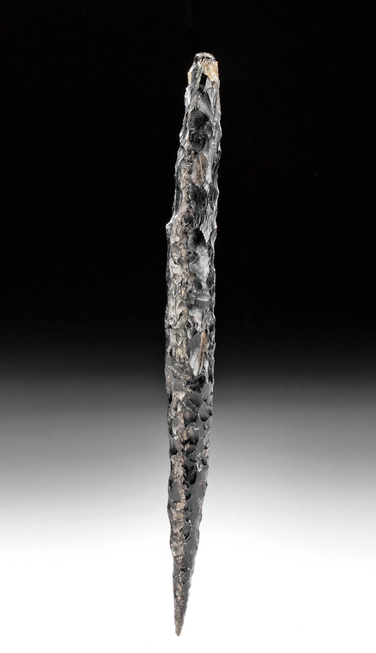 Pre-Columbian Colima Obsidian Spear Head: Pre-Columbian, West Mexico, Colima, ca. 300 BCE to 300 CE. A slender spear head of a minimalist form that is hand-knapped from opaque obsidian of a jet-black hue. The blade has a flat base with a roun