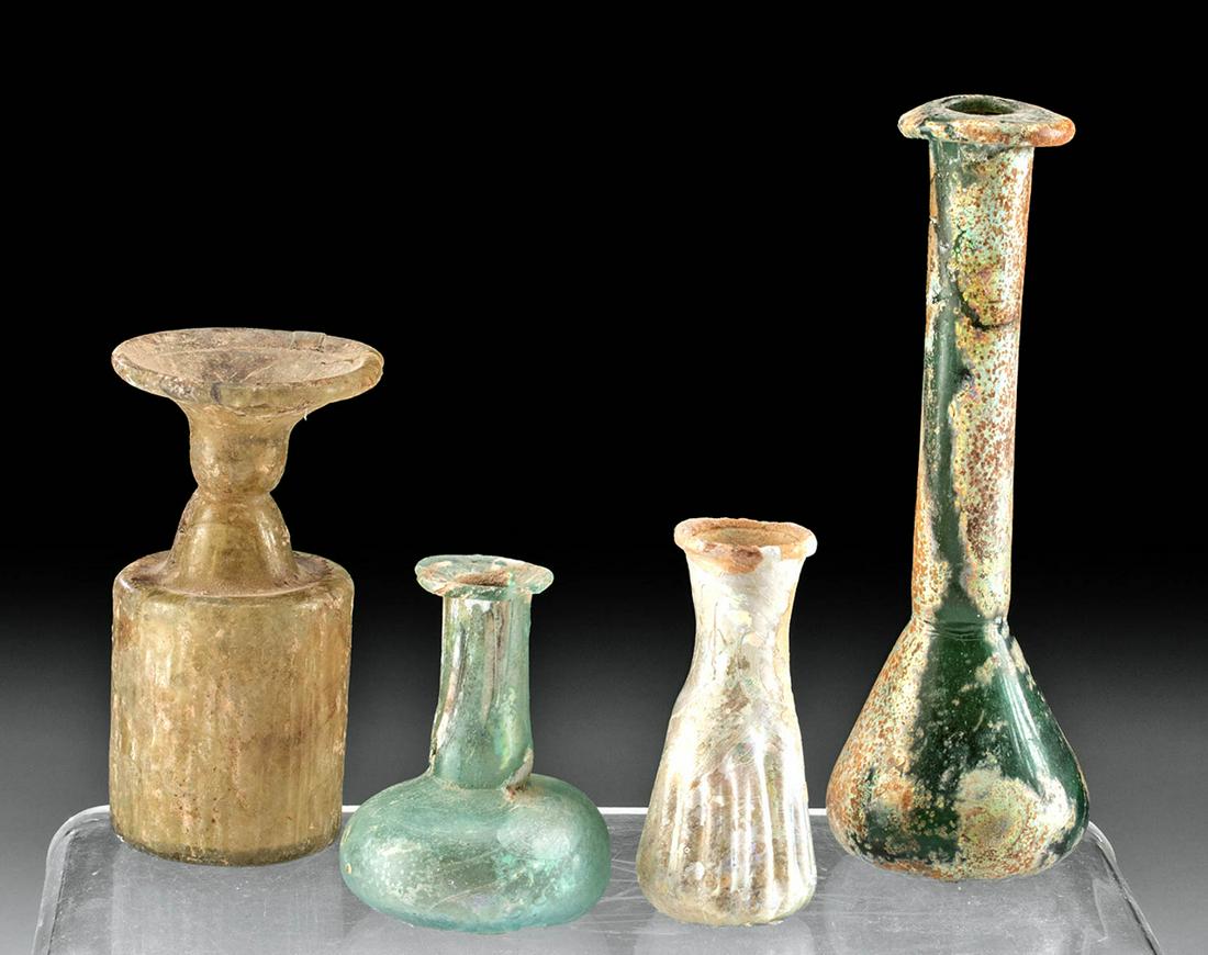 Lot of 4 Roman Glass Bottles: Roman, Imperial Period, ca. 1st to 3rd century CE. A collection of four lovely glass vessels with a variety of shapes. The first and tallest is an unguentarium with an aqua hue, a teardrop shaped body