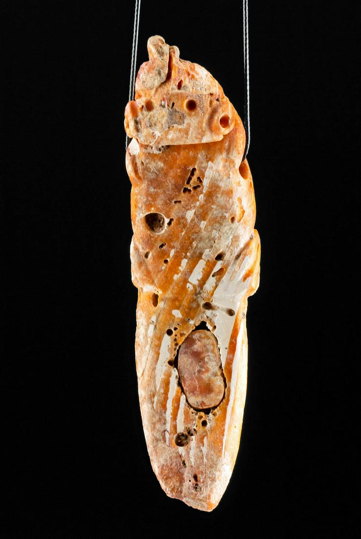 Colima Spondylus Shell Crocodile Purging Stick Pendant: Pre-Columbian, West Mexico, Colima culture, ca. 300 BCE to 300 CE. A hand-carved Spondylus shell pendant, with a beige and orange hue, the overall form of a purging stick, and zoomorphic features. The