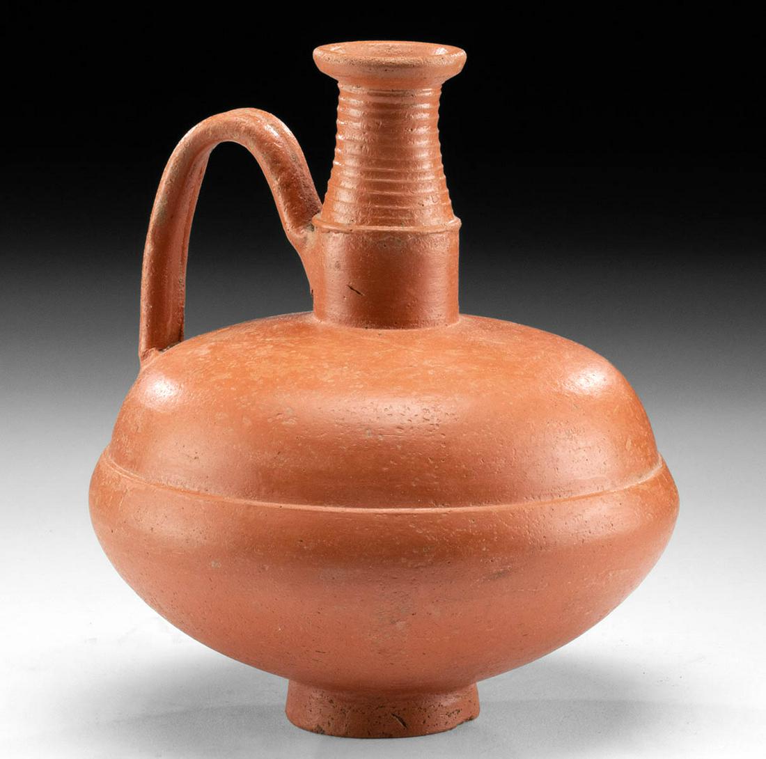 Roman North African Footed Flagon, ex-Charles Ede: Roman, North Africa, Imperial period, ca. 2nd century CE. A wheel-thrown slipware pottery flagon exhibiting vibrant remains of the original red-orange color. The bulbous vessel features a compressed b