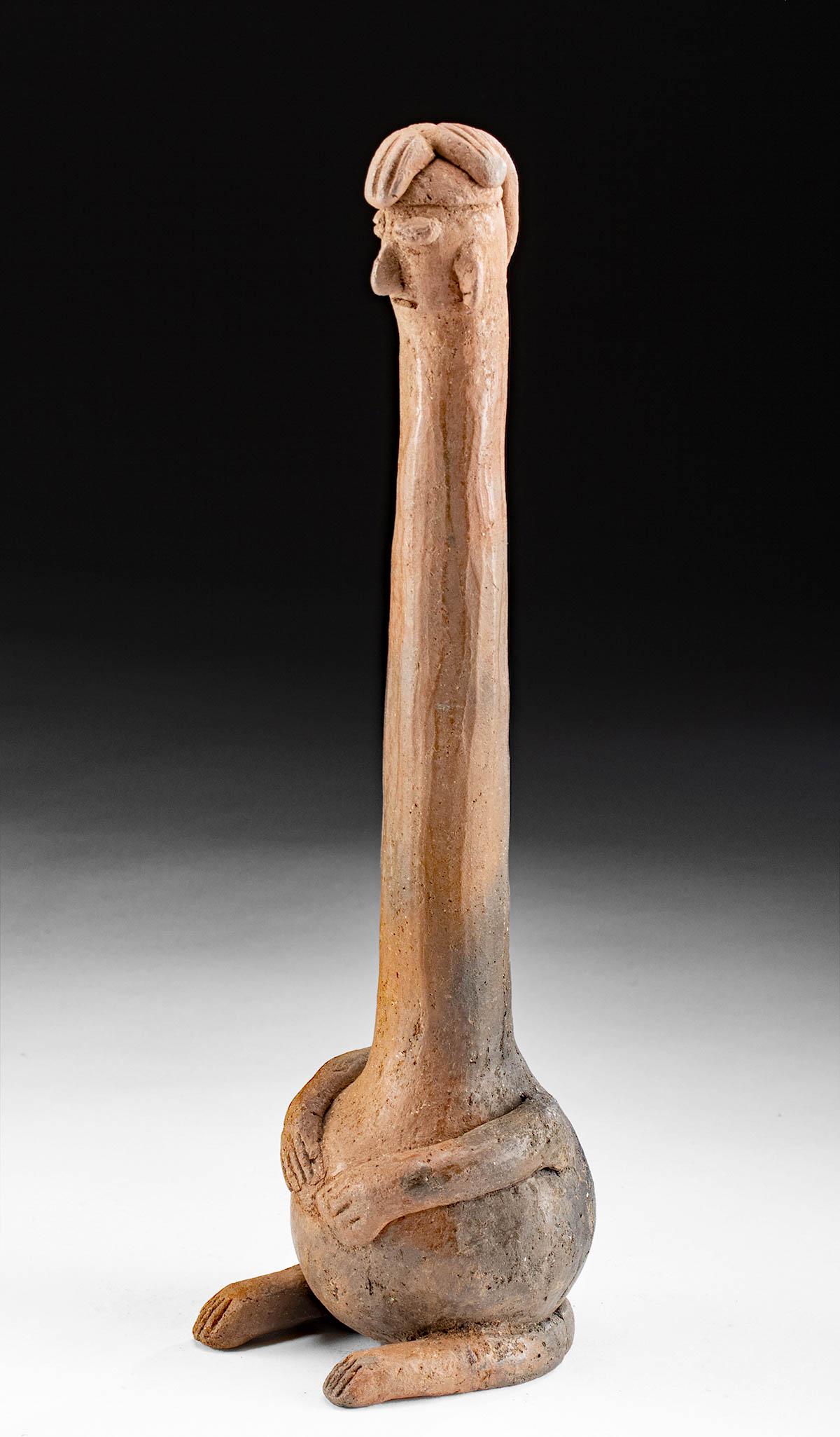 Colima Pottery Figural Musical Rattle: Pre-Columbian, West Mexico, Colima, Protoclassic Period, ca. 100 BCE to 250 CE. A fun redware pottery rattle in the form of a seated figure presenting a spherical body and a very long, attenuated neck