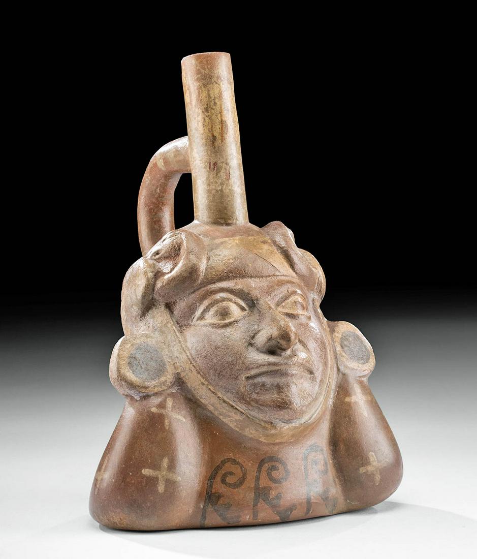 Moche Polychrome Portrait Vessel w/ Avian Headdress: Pre-Columbian, North Coast Peru, Moche III to IV, ca. 450 to 650 CE. A fabulous mold-made earthenware portrait stirrup vessel depicting a visage of a young man, likely a shaman or lord, donning a fanc