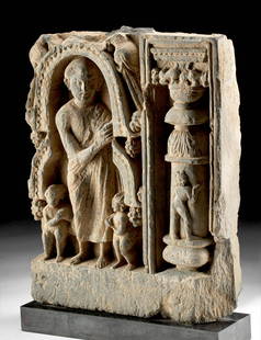 Gandharan Schist Relief Panel w/ Man, Putti, and Column: Northwest Pakistan, Gandharan Empire, ca. 2nd to 3rd century CE. A remarkable schist panel depicting a standing man surrounded by a pair of putti next to an ornate column, all skillfully carved in