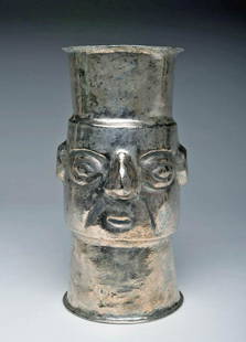 Chimu Silver Kero / Drinking Vessel Figural Detailing: Pre-Columbian, Peru, Chimu, ca. 1000 to 1200 CE. A silver kero or drinking vessel hammered into a beaker shape with a flat base and flaring sides with a handsome visage created in repousse